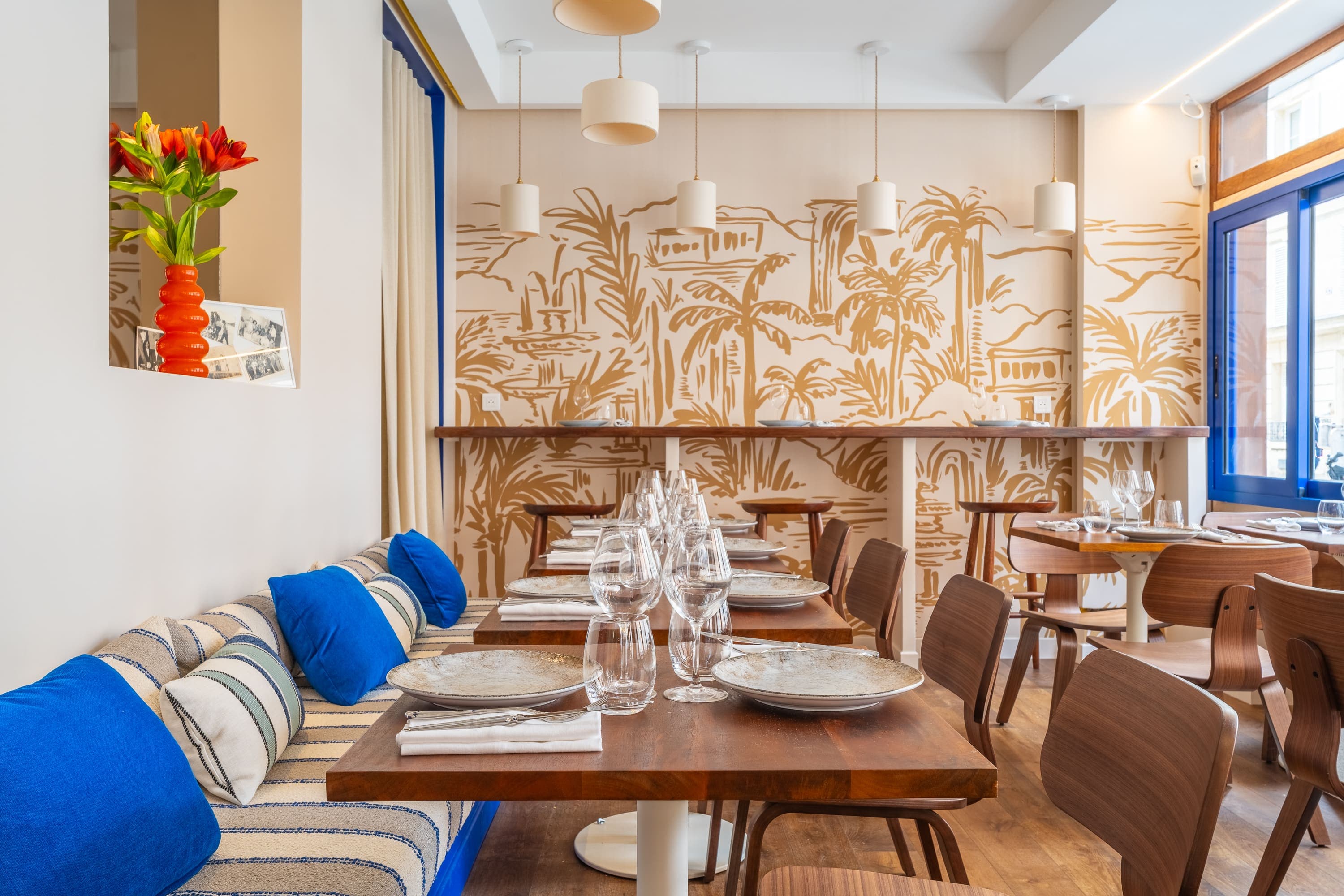 Salle du restaurant Lucien, tables dressées devant une fresque murale de palmiers.